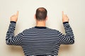 Hispanic man wearing a striped sweater pointing up with index fingers with his back to the camera, isolated on beige