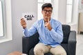 Hispanic man working at therapy office holding call me banner serious face thinking about question with hand on chin, thoughtful Royalty Free Stock Photo