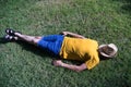 Hispanic mature adult male lying on the grass sleeping with a hat on his face