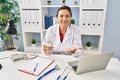 Hispanic mature doctor woman holding pill and glass of water smiling looking to the side and staring away thinking Royalty Free Stock Photo