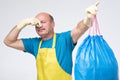 Hispanic mature male closing his nose and carrying a stinky garbage bag