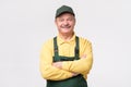 Hispanic mature mechanic in green cap and overalls standing smiling