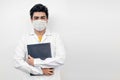 Hispanic medical student wearing a facemask and a medical robe and holding his textbook