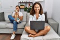 Hispanic middle age couple at home, woman using laptop happy face smiling with crossed arms looking at the camera Royalty Free Stock Photo