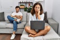 Hispanic middle age couple at home, woman using laptop thinking looking tired and bored with depression problems with crossed arms Royalty Free Stock Photo