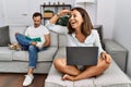 Hispanic middle age couple at home, woman using laptop very happy and smiling looking far away with hand over head Royalty Free Stock Photo