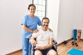 Hispanic middle age man sitting on wheelchair and nurse at rehabilitation clinic looking positive and happy standing and smiling Royalty Free Stock Photo