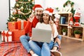 Hispanic middle age woman and mature man using laptop sitting by christmas tree surprised with an idea or question pointing finger Royalty Free Stock Photo