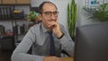 Hispanic middle-aged man in glasses working in a modern office, focused intently on his computer screen with a thoughtful Royalty Free Stock Photo