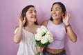 Hispanic mother and daughter holding bouquet of white flowers smiling with hand over ear listening an hearing to rumor or gossip Royalty Free Stock Photo