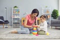 Hispanic mother and daughter play with toys while sitting on the floor in the room.