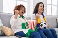 Hispanic mother and daughter watching football supporting team screaming proud, celebrating victory and success very excited with Royalty Free Stock Photo