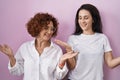 Hispanic mother and daughter wearing casual white t shirt over pink background smiling showing both hands open palms, presenting Royalty Free Stock Photo