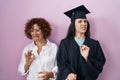 Hispanic mother and daughter wearing graduation cap and ceremony robe disgusted expression, displeased and fearful doing disgust Royalty Free Stock Photo
