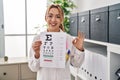 Hispanic optician woman holding medical exam doing ok sign with fingers, smiling friendly gesturing excellent symbol Royalty Free Stock Photo