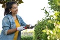 Hispanic real woman smiling and working on the yard cutting bush with hedge shear at home