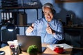 Hispanic senior man wearing call center agent headset at night approving doing positive gesture with hand, thumbs up smiling and Royalty Free Stock Photo