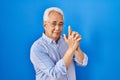 Hispanic senior man wearing glasses holding symbolic gun with hand gesture, playing killing shooting weapons, angry face Royalty Free Stock Photo