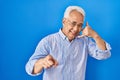 Hispanic senior man wearing glasses smiling doing talking on the telephone gesture and pointing to you Royalty Free Stock Photo