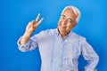 Hispanic senior man wearing glasses smiling looking to the camera showing fingers doing victory sign Royalty Free Stock Photo