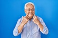 Hispanic senior man wearing glasses smiling with open mouth, fingers pointing and forcing cheerful smile Royalty Free Stock Photo