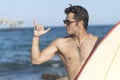 Hispanic surfer boy standing on the beach in wetsuit holding his blue surfboard and doing the surf salute Royalty Free Stock Photo