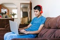 Hispanic teenage boy with headphones listening to music while using laptop at home in Latin America Royalty Free Stock Photo
