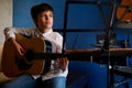 Hispanic teenage boy in white casual shirt, plucking strings while strumming guitar, playing acoustic classic guitar Royalty Free Stock Photo