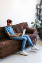 Hispanic teenager boy with headphones sitting on sofa while using laptop at home in Latin America Royalty Free Stock Photo