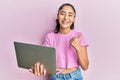 Hispanic teenager girl with dental braces holding and using computer laptop pointing thumb up to the side smiling happy with open Royalty Free Stock Photo