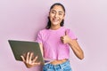 Hispanic teenager girl with dental braces holding and using computer laptop smiling happy and positive, thumb up doing excellent Royalty Free Stock Photo