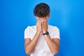 Hispanic teenager standing over blue background rubbing eyes for fatigue and headache, sleepy and tired expression