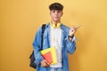 Hispanic teenager wearing student backpack and holding books with a big smile on face, pointing with hand finger to the side Royalty Free Stock Photo