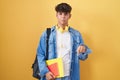 Hispanic teenager wearing student backpack and holding books pointing down looking sad and upset, indicating direction with Royalty Free Stock Photo