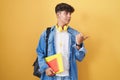 Hispanic teenager wearing student backpack and holding books smiling with happy face looking and pointing to the side with thumb Royalty Free Stock Photo