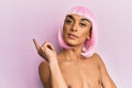 Hispanic transgender man wearing make up and pink wig smiling happy pointing with hand and finger to the side