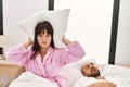 Hispanic woman angry with pillow on his ears while man snoring on the bed Royalty Free Stock Photo