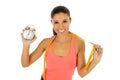 Hispanic woman holding alarm clock and taylor measure tape in time for sport and diet concept Royalty Free Stock Photo