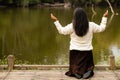 Woman Kneeling in Prayer in Front of River in Forest Preserve