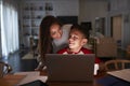 Hispanic woman looking over her sonÃ¯Â¿Â½s shoulder while he does his homework using laptop computer