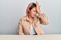 Hispanic woman with pink hair wearing casual clothes sitting on the table surprised with hand on head for mistake, remember error