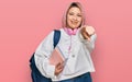 Hispanic woman with pink hair wearing student backpack and headphones pointing to you and the camera with fingers, smiling Royalty Free Stock Photo