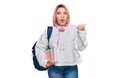 Hispanic woman with pink hair wearing student backpack and headphones surprised pointing with hand finger to the side, open mouth Royalty Free Stock Photo