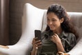 Hispanic woman relaxing on armchair holds cellphone read pleasant sms Royalty Free Stock Photo