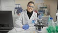 Hispanic woman scientist smiling in laboratory with microscope, flasks, and computer Royalty Free Stock Photo