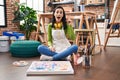 Hispanic woman sitting at art studio painting on canvas pointing finger up with successful idea Royalty Free Stock Photo