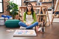 Hispanic woman sitting at art studio painting on canvas with serious expression on face Royalty Free Stock Photo