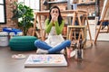 Hispanic woman sitting at art studio painting on canvas shocked covering mouth with hands for mistake Royalty Free Stock Photo