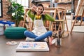 Hispanic woman sitting at art studio painting on canvas smiling making frame with hands and fingers with happy face Royalty Free Stock Photo