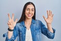 Hispanic woman standing over blue background showing and pointing up with fingers number eight while smiling confident and happy Royalty Free Stock Photo